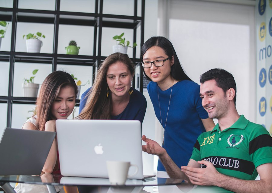 A smiling group of people working together around a laptop